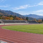 紅葉した山並みを背景にした陸上競技場のトラックとスタンド