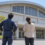 地域の体育館を見上げる担当者2人の後ろ姿
