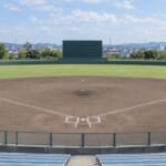 地方都市の野球場。内野の土と外野の芝、奥に山並み