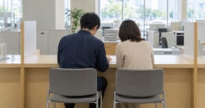 市役所の窓口カウンターで相談する2人の後ろ姿