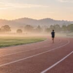 朝もやの陸上トラックを走る選手の後ろ姿